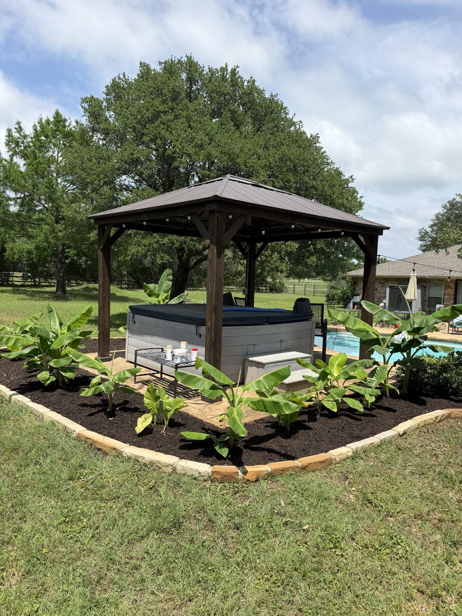Gazebo and hot tub framed by a tropical landscape bed with stone border